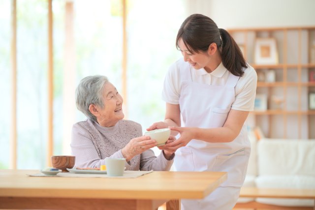 介護施設で高齢者にお茶碗を渡す介護職員